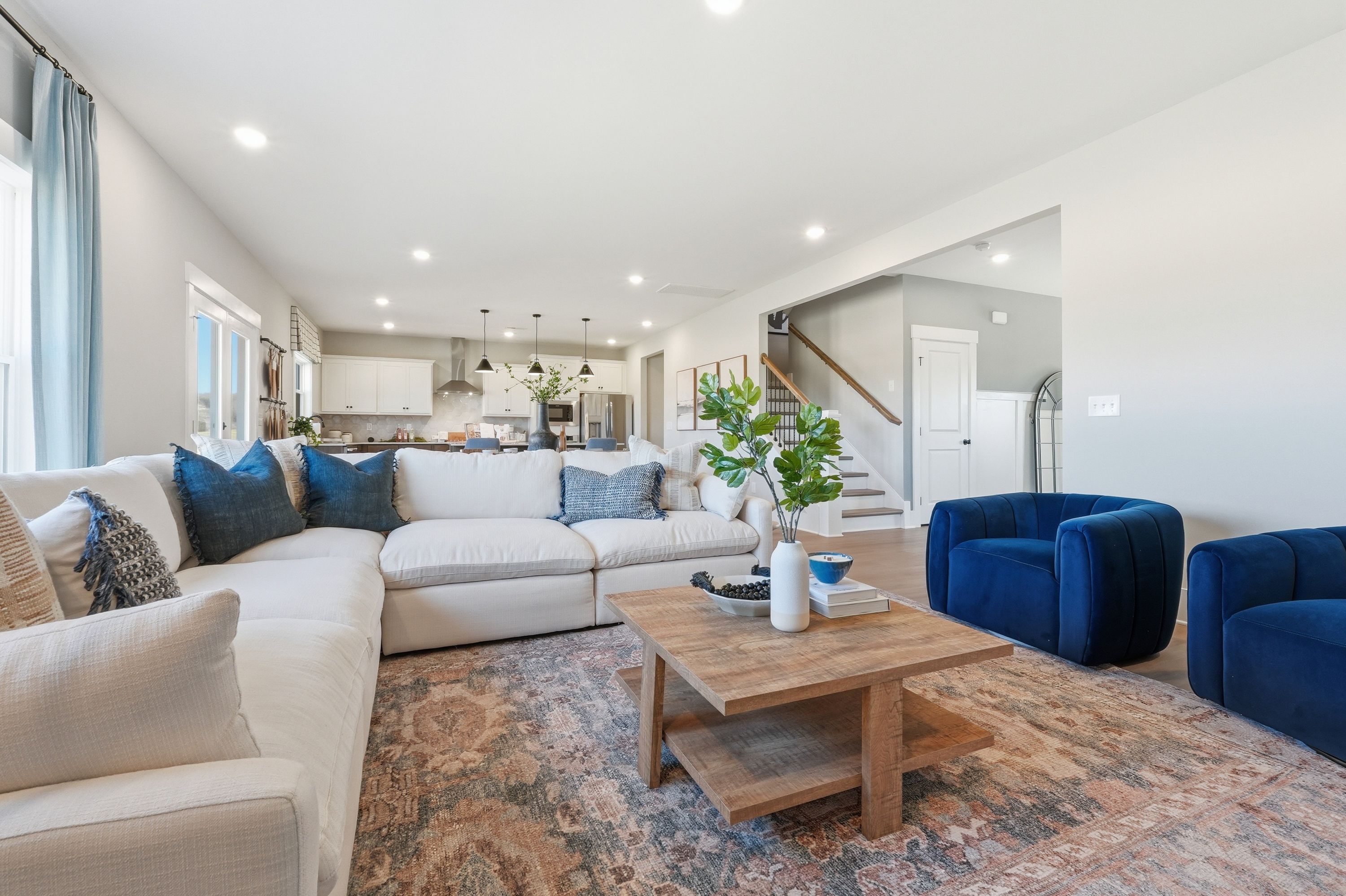 Cozy open-concept living room in Berry Cove New Market Alabama with L-shaped white sofa, blue pillows, wooden coffee table, and kitchen view