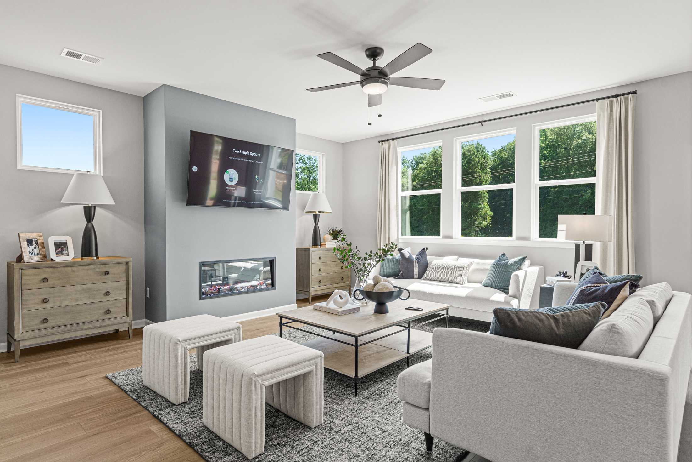 Open-concept living room at Fern Hollow in Buford Georgia with white sofas fireplace mounted TV hardwood floors and large windows