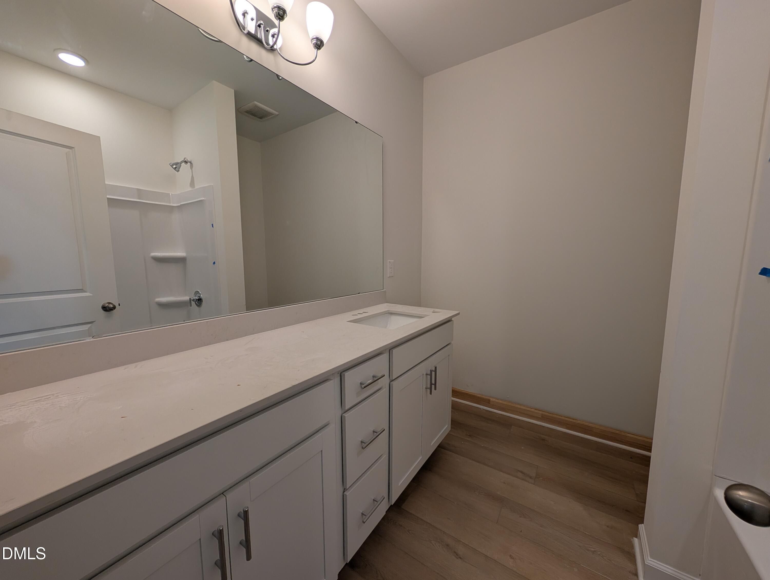 Bathroom with white vanity, quartz countertop, large mirror, and wood-look flooring in Davidson Homes The Magnolia A, Wendell Ridge