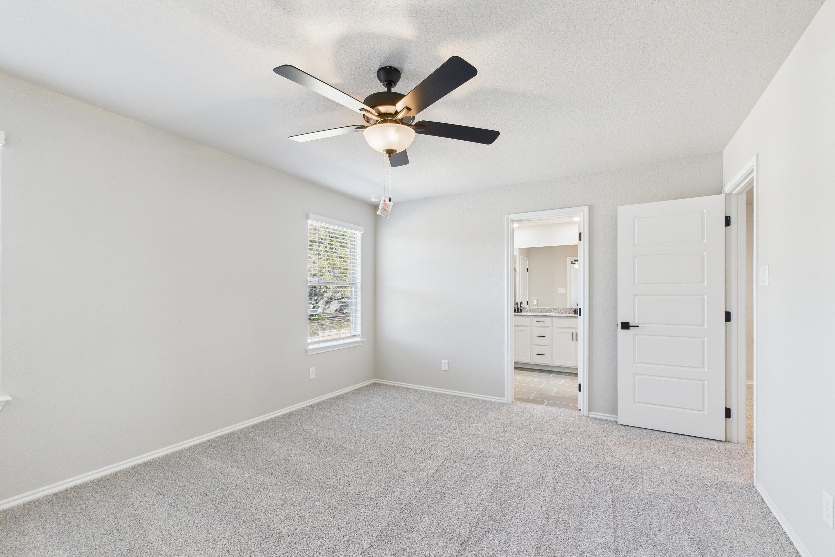 Spacious upper-floor bedroom in The Charlotte A home design featuring neutral carpet, ceiling fan, and access to ensuite.