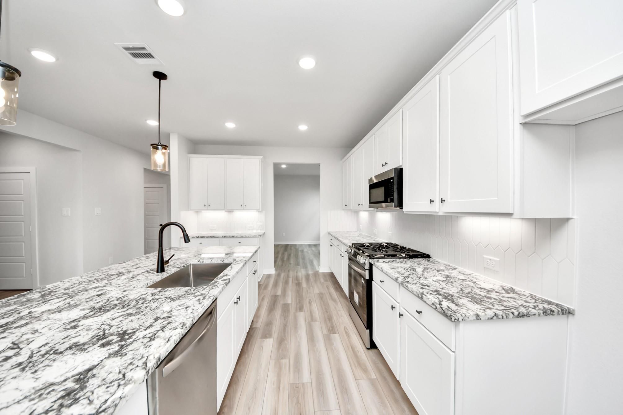 Modern kitchen with white cabinets, granite countertops, and stainless appliances in The Sorrento E at Sundance Cove, Crosby.