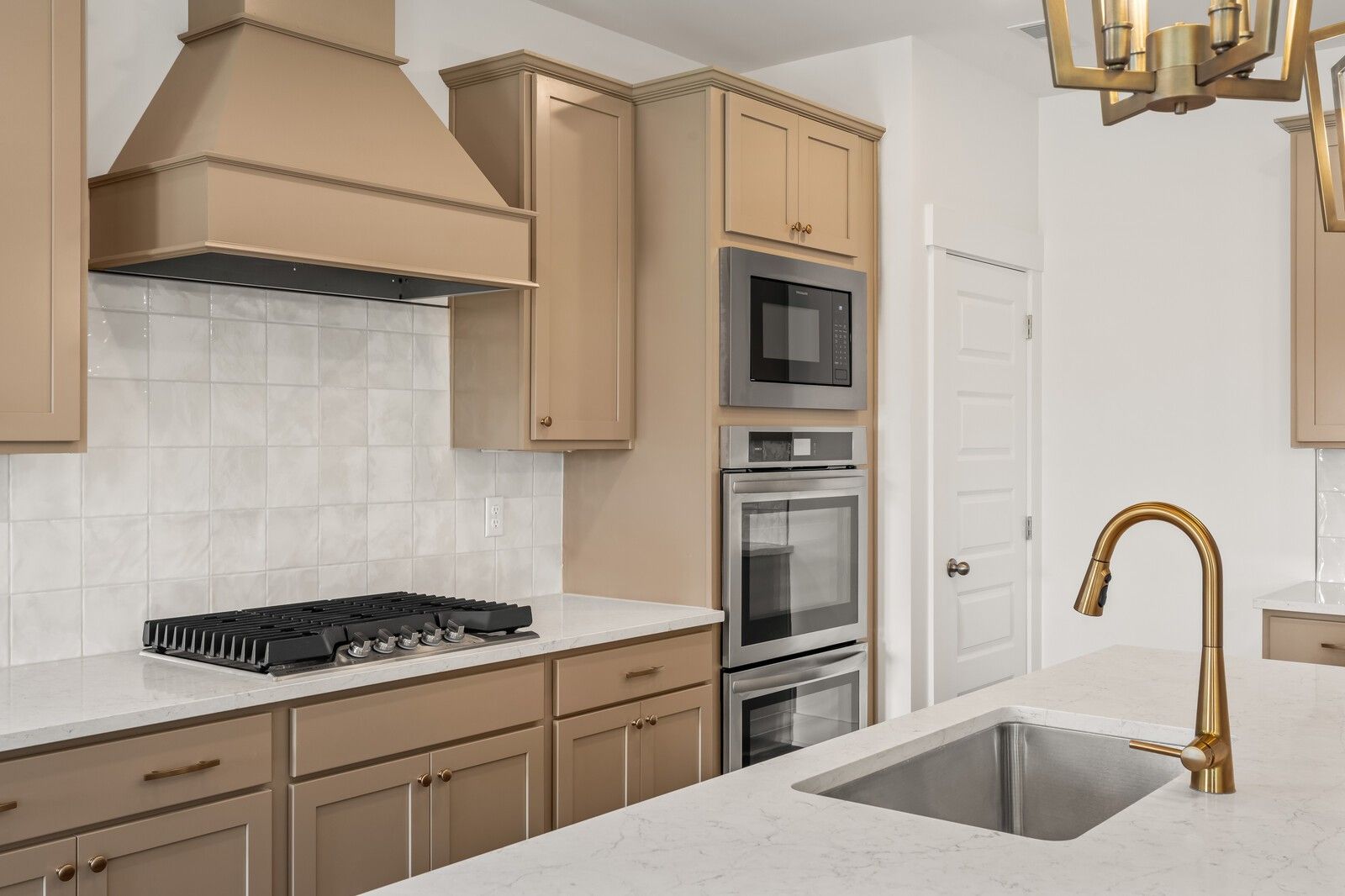 Modern kitchen featuring beige shaker cabinets, white subway tile backsplash, gas cooktop, double ovens, and gold faucet in Davidson Homes The Ash A, Gallatin, TN