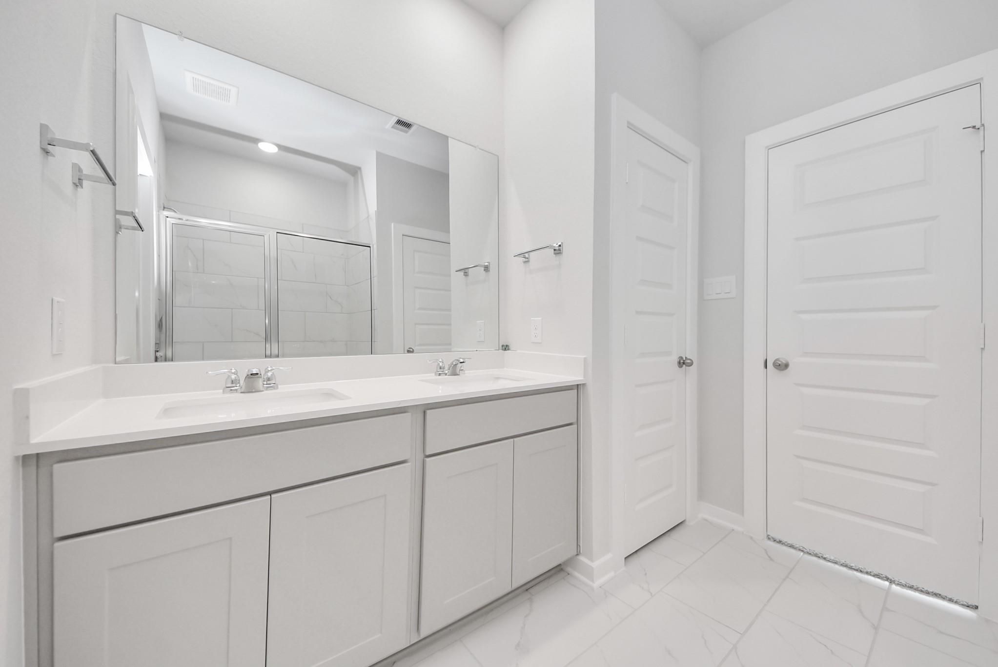 Modern dual-sink bathroom vanity with white countertops in The Blanco F floor plan at Spring Branch Crossing in Conroe.