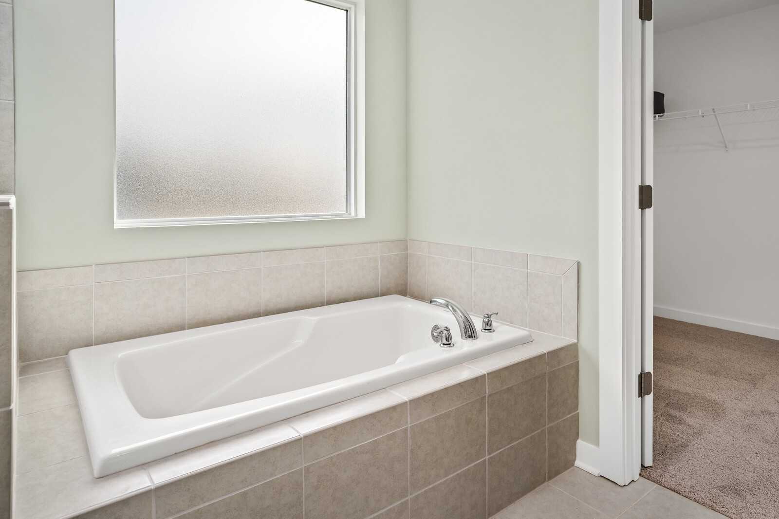 Modern bathroom with deep soaking tub, tiled surround, and frosted window in Davidson Homes The Gordon C, White House, TN