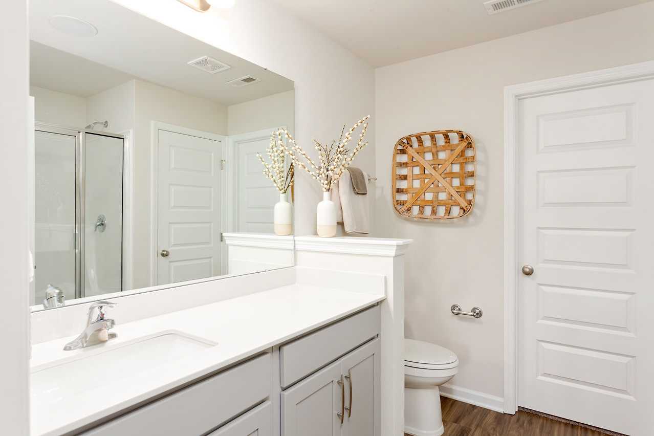 Elegant master bathroom in The Franklin featuring white double vanity, frameless glass shower, and woven decor with branches