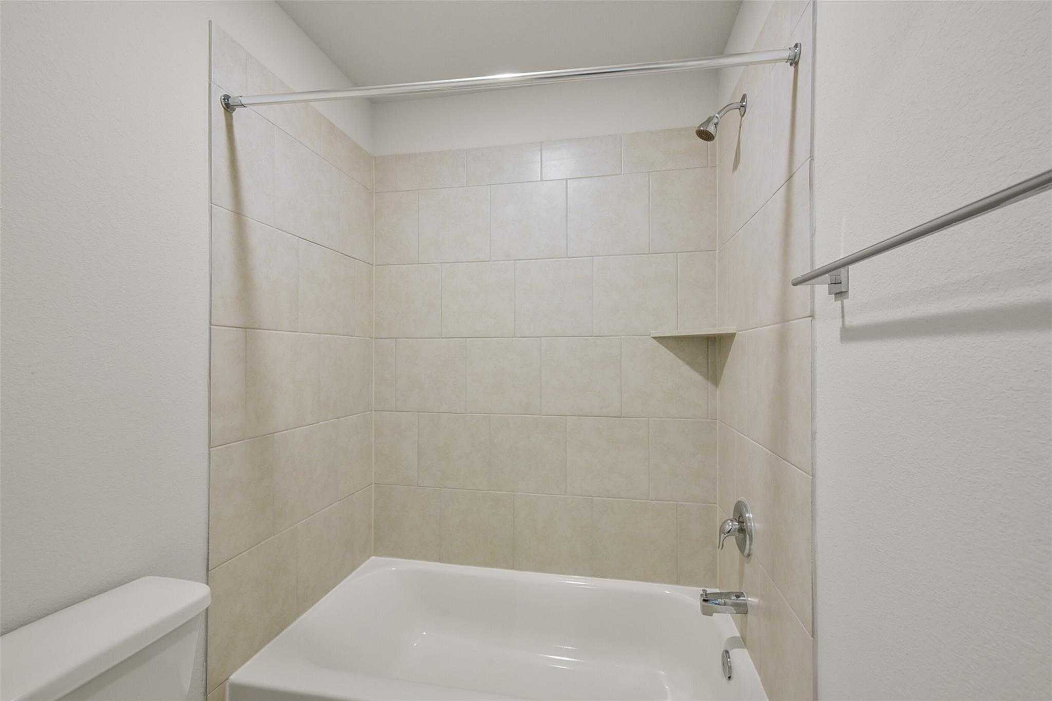 Modern beige-tiled shower with glass enclosure and soaking tub in 4-bedroom Davidson Homes Sabine E, Dayton, Texas