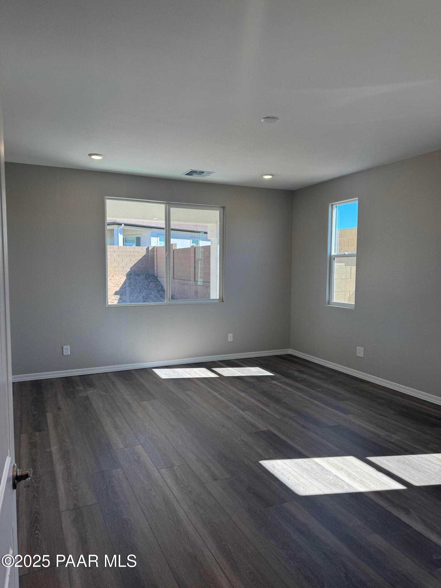 Spacious bedroom with light gray walls, large windows, sunlight streaming on hardwood floors in Davidson Homes The Monarch E, Prescott Arizona