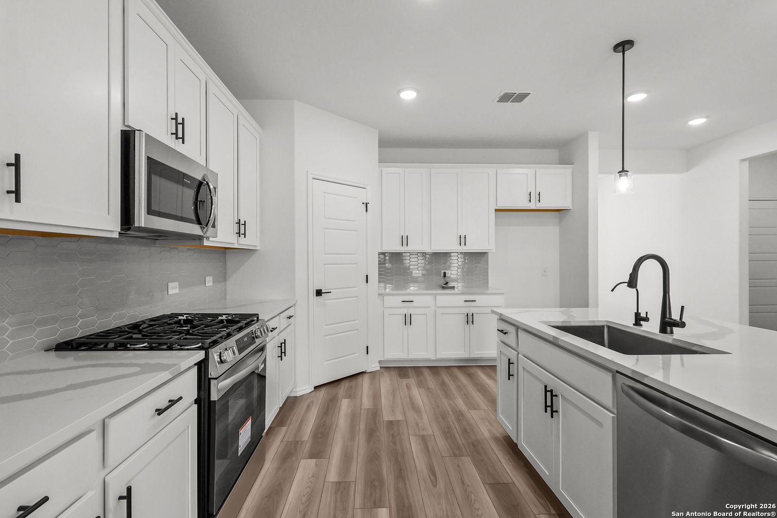 Modern white kitchen with quartz island, stainless appliances, subway tile backsplash in Davidson Homes The Douglas E, San Antonio