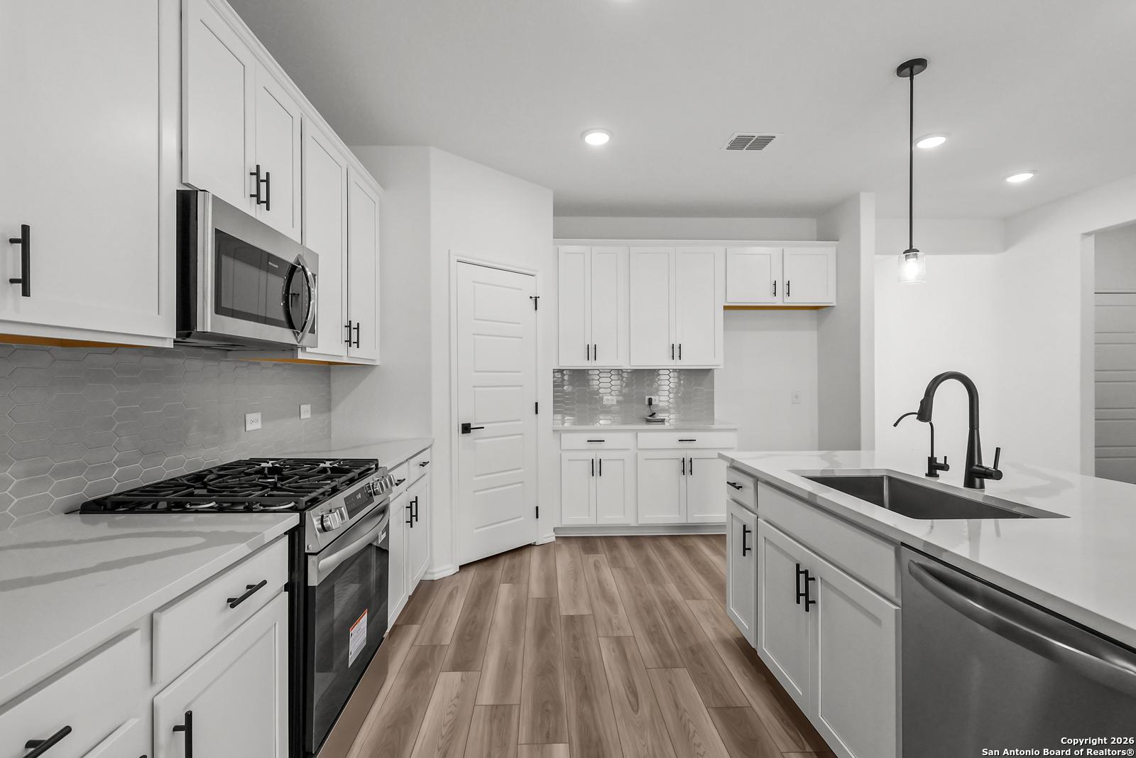 Modern white kitchen with quartz island, stainless appliances, subway tile backsplash in Davidson Homes The Douglas E, San Antonio