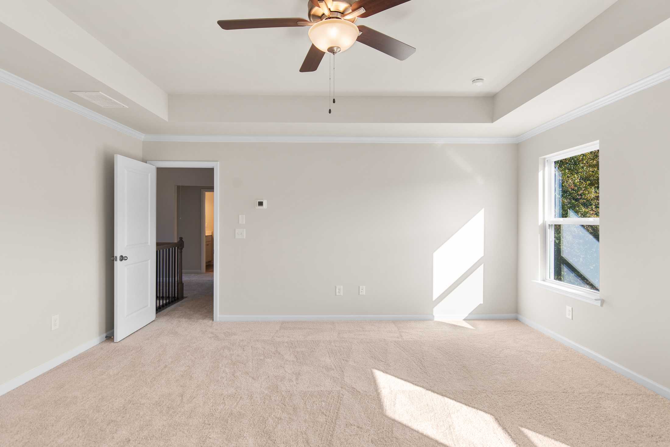 Spacious master bedroom in The Willow B at Wehunt Meadows, Hoschton GA, featuring ceiling fan, tray ceiling, and sunlit window