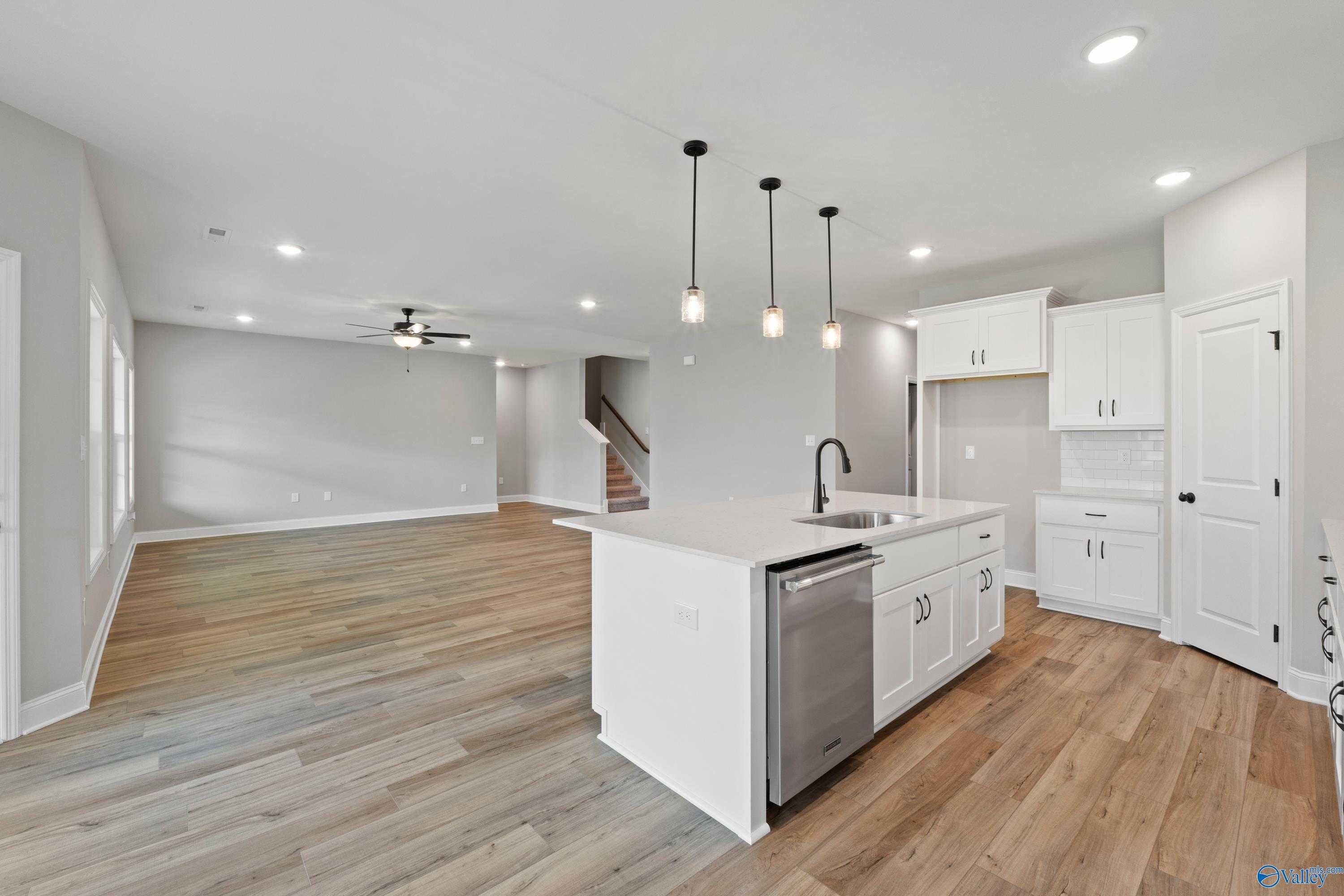 Modern open-concept kitchen with white island, stainless sink, dishwasher, pendant lights, and wood floors in Davidson Homes The Rockford, Toney, Alabama