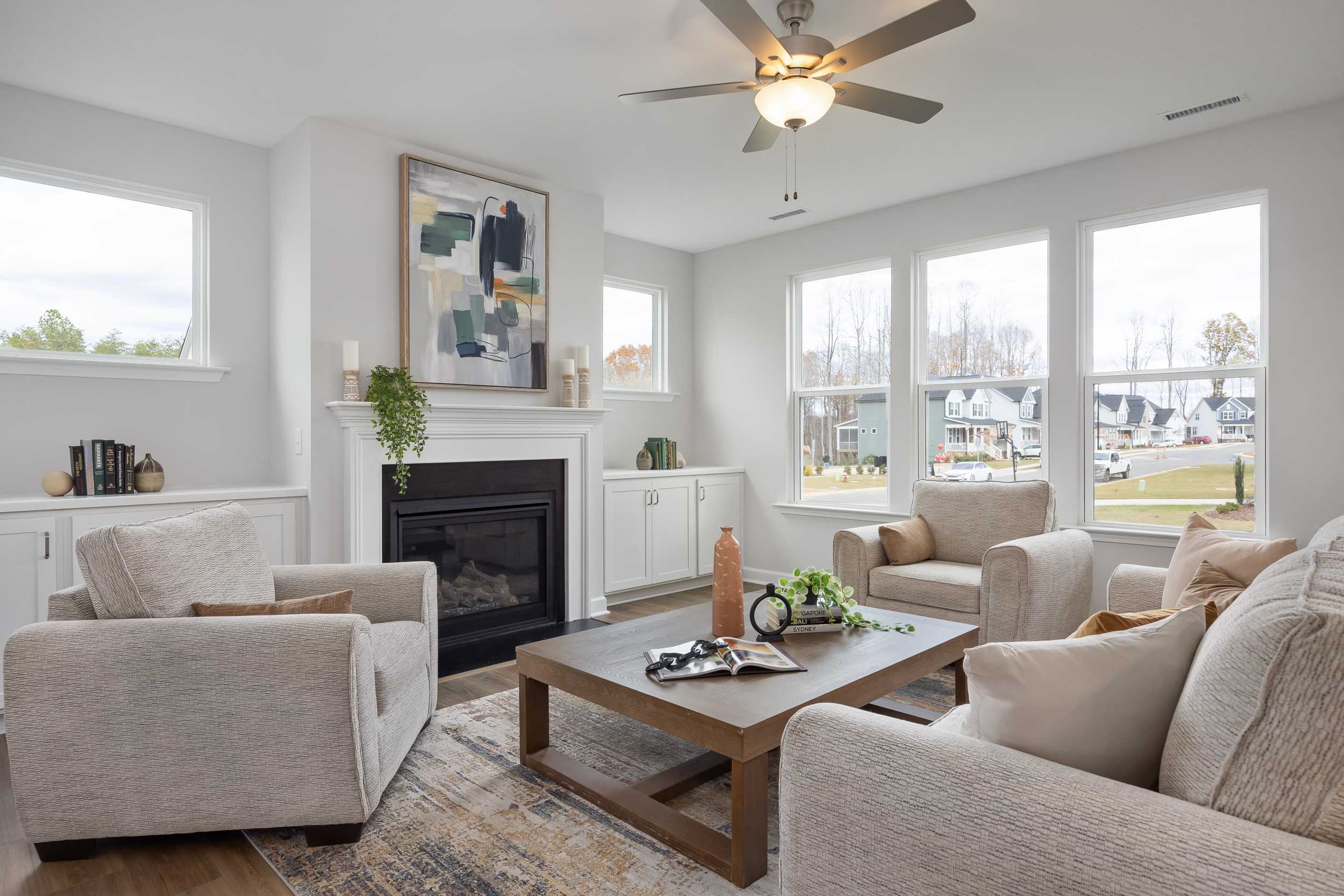 Spacious living room at Enclave at Belmont in Belmont NC featuring gas fireplace, cream sofas, ceiling fan, and large windows