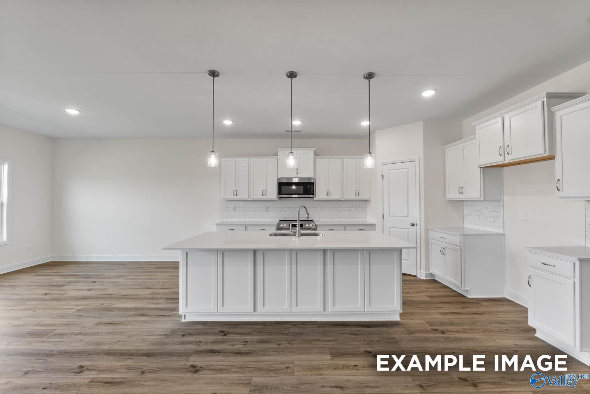 Bright modern kitchen with white cabinets, large center island, stainless appliances, and hardwood floors in Davidson Homes The Harrison C, Athens AL