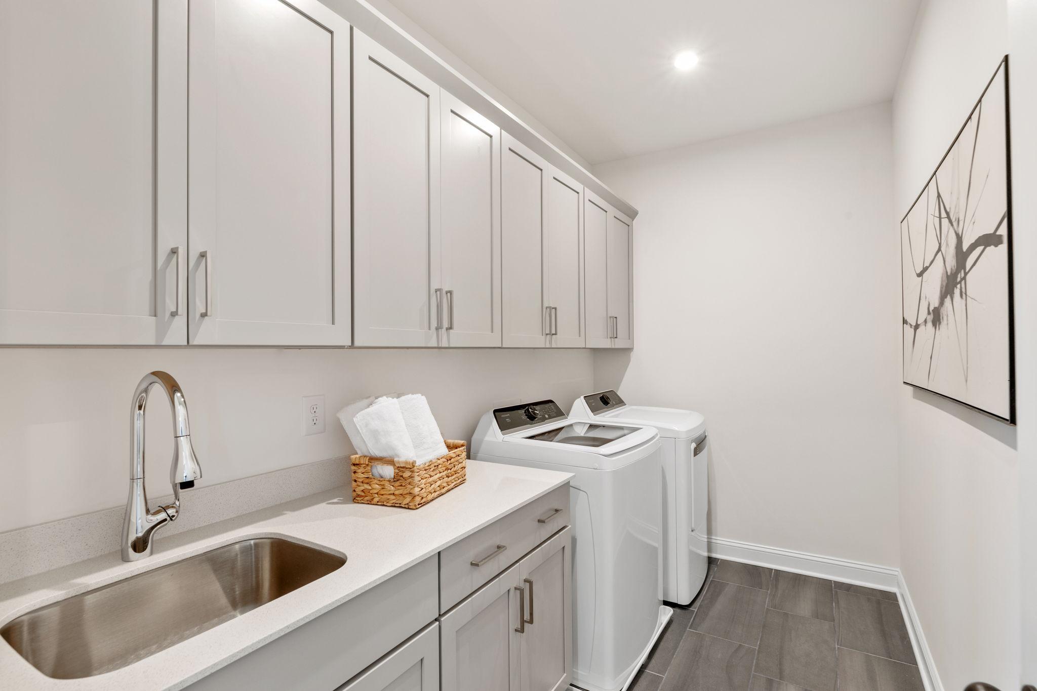 Spacious laundry room in Fern Hollow Buford GA by Davidson Homes featuring white shaker cabinets washer dryer and utility sink
