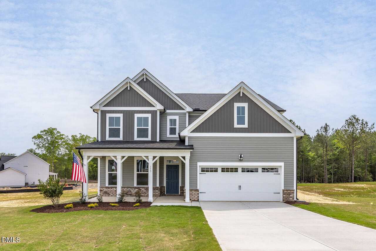 Two-story gray Craftsman home with wraparound porch, American flag, and 2-car garage in Woodland Crossing, Zebulon, NC by Davidson Homes