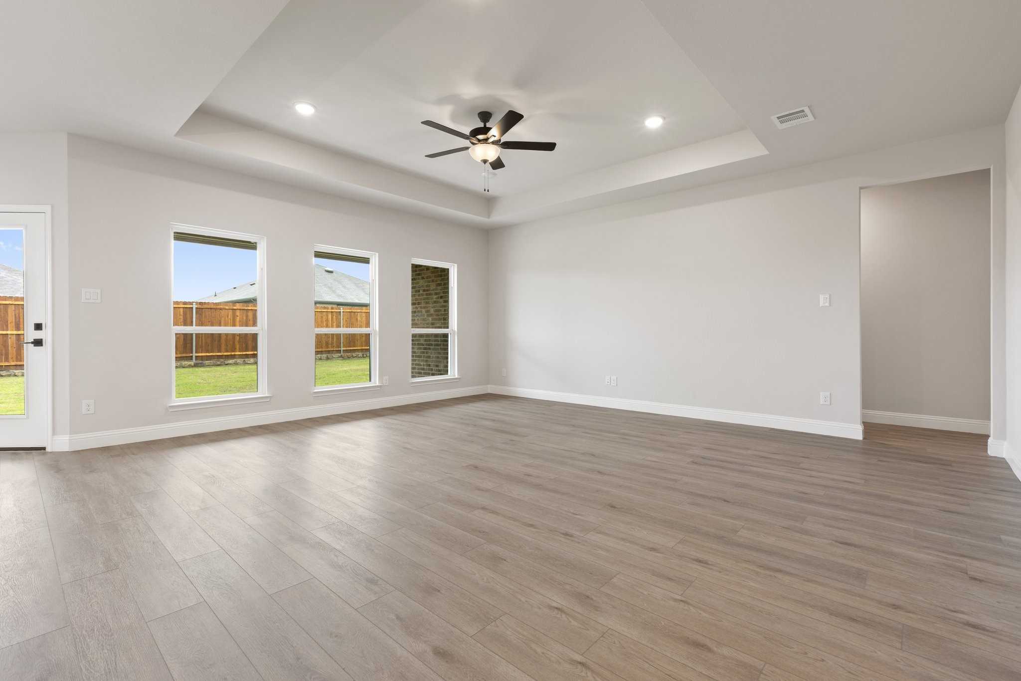 Spacious living room with light wood flooring, large windows to green yard, ceiling fan in Davidson Homes The Harrison D, Josephine Texas