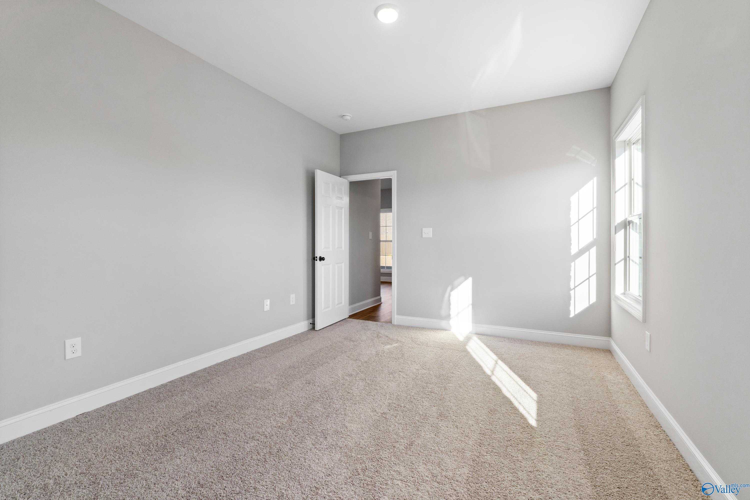 Bright secondary bedroom with gray walls, beige carpet, and large sunny windows in The Valencia 4-bedroom home, Meridianville, Alabama
