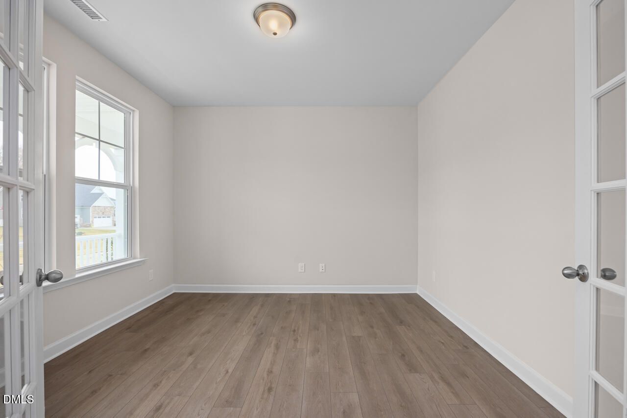 Bright empty bedroom with hardwood floors, French doors, and large windows in Davidson Homes The Cypress D II, Angier, NC