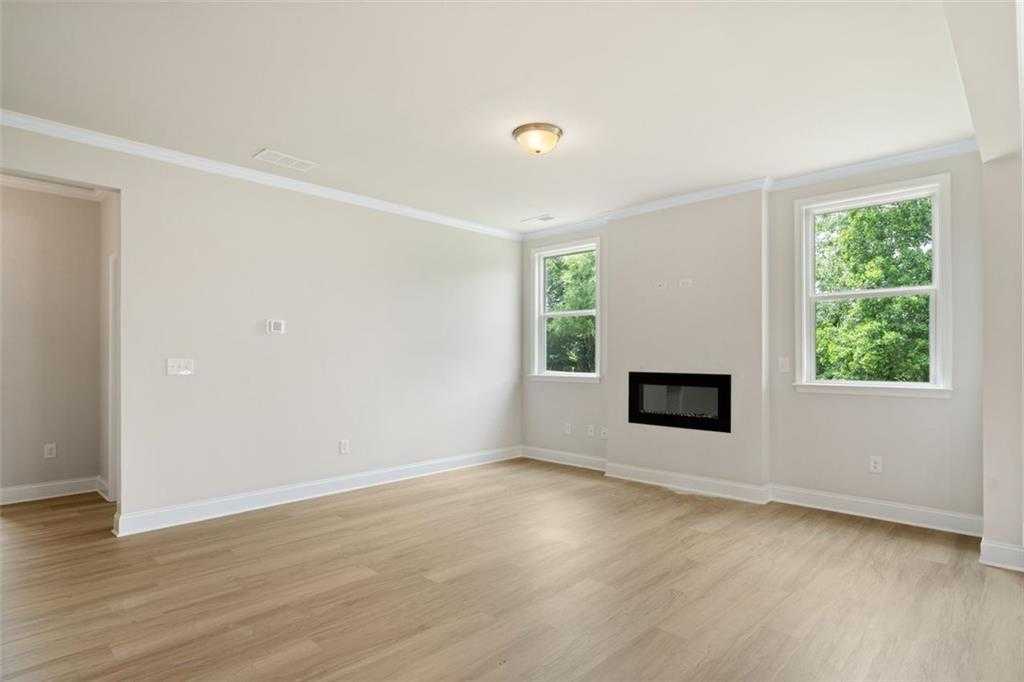 Bright living room with modern linear fireplace, large windows overlooking trees, hardwood floors in The Willow D at Wehunt Meadows, Hoschton
