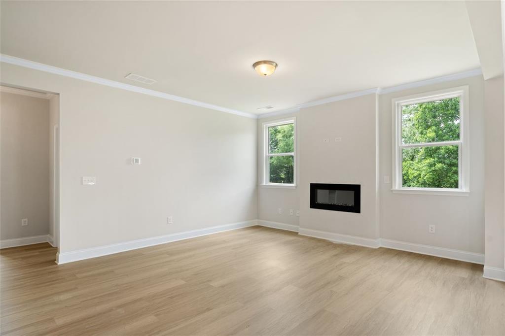 Bright living room with modern linear fireplace, large windows overlooking trees, hardwood floors in The Willow D at Wehunt Meadows, Hoschton