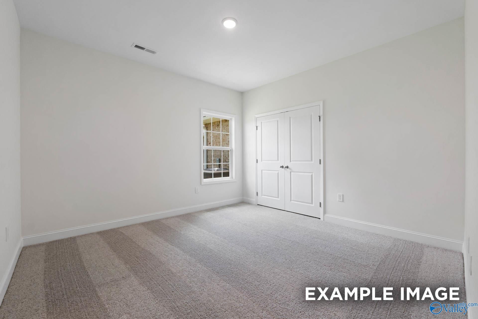 Bright secondary bedroom with white walls, large window, double closet doors, and neutral carpet in Davidson Homes The Oxford, Huntsville