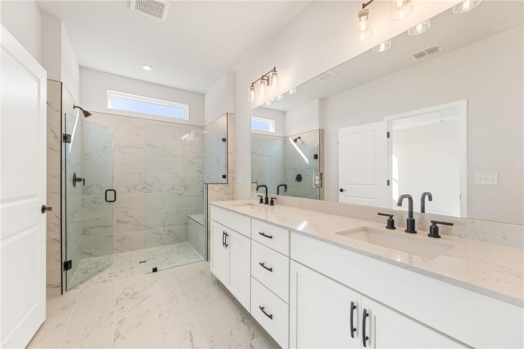Luxurious master bathroom with double vanity, quartz counters, and frameless glass shower in The Glenwood C, Loganville, GA