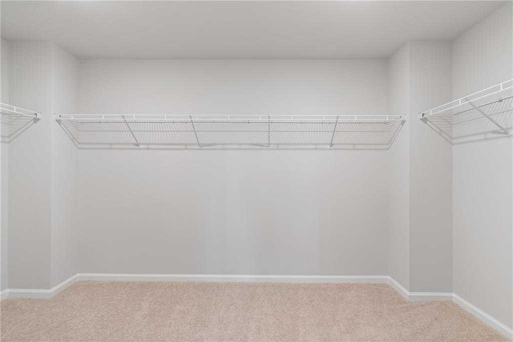 Spacious walk-in closet with white wire shelving on three walls and beige carpet in The Hickory B by Davidson Homes, Winder, GA