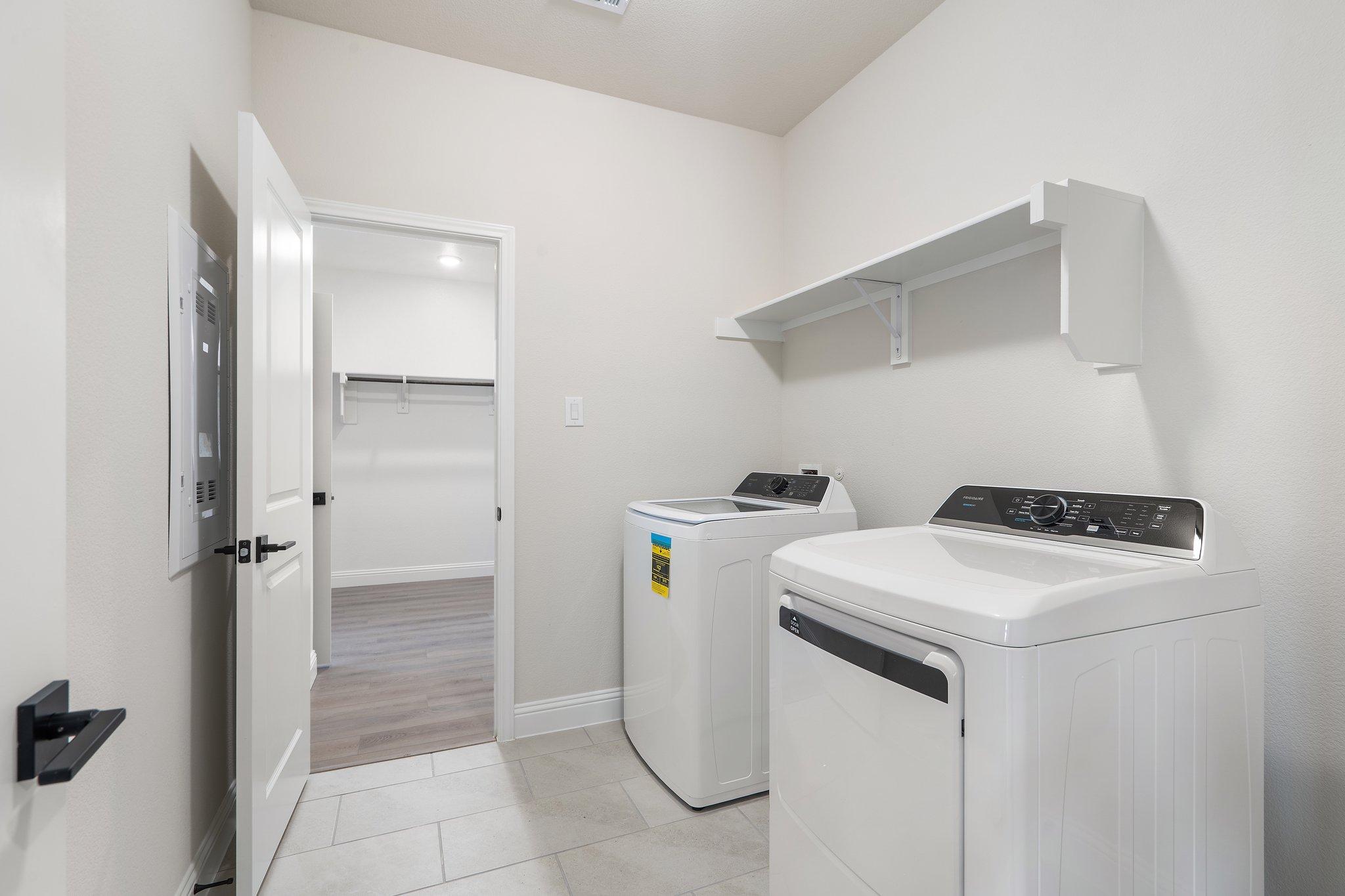 Laundry room in The Holly F home design featuring white appliances, wall shelving, and an adjacent walk-in closet.