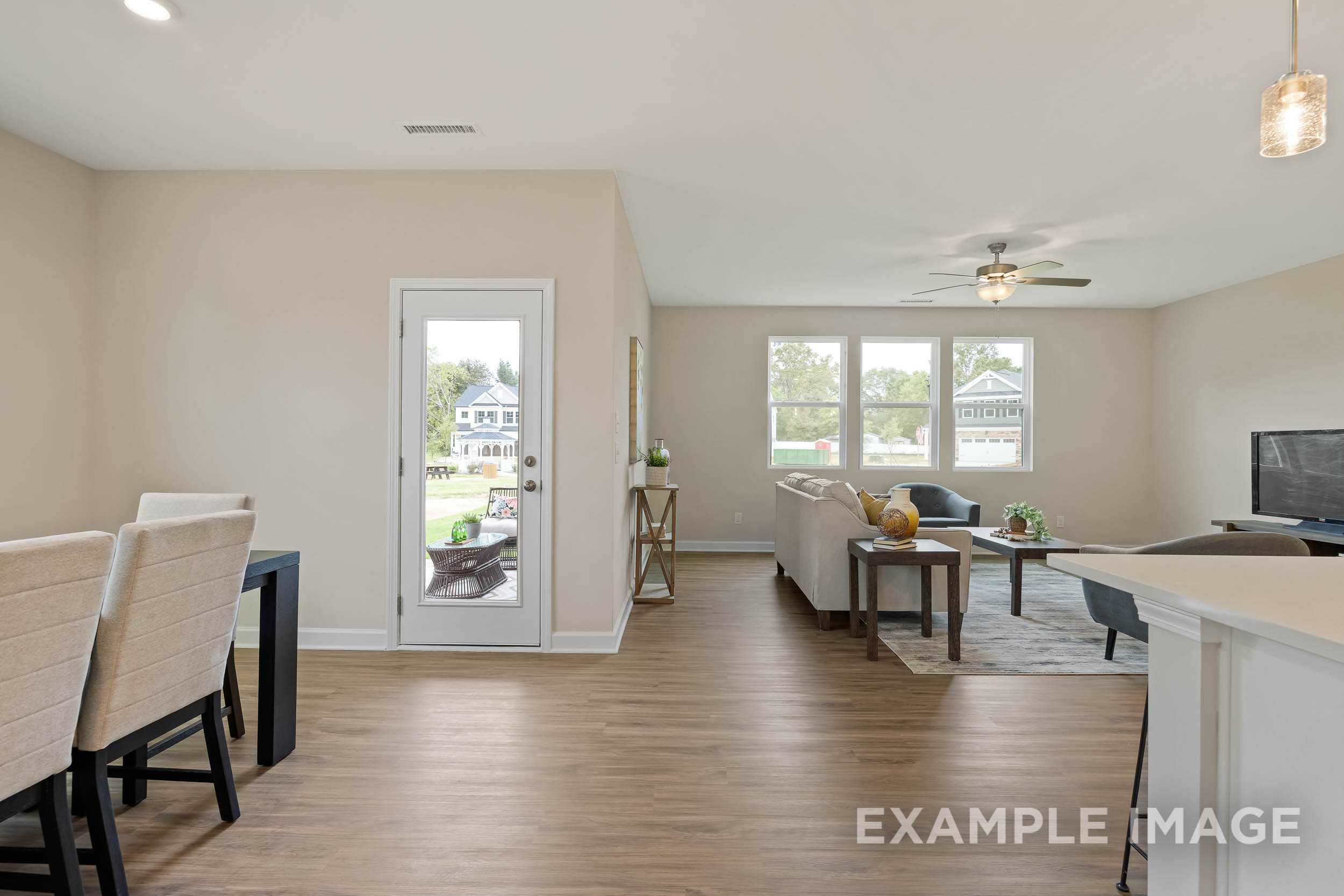 Open-concept living room and kitchen in The Preston B with neutral walls, wood floors, beige sofa, ceiling fan, and sliding door to backyard
