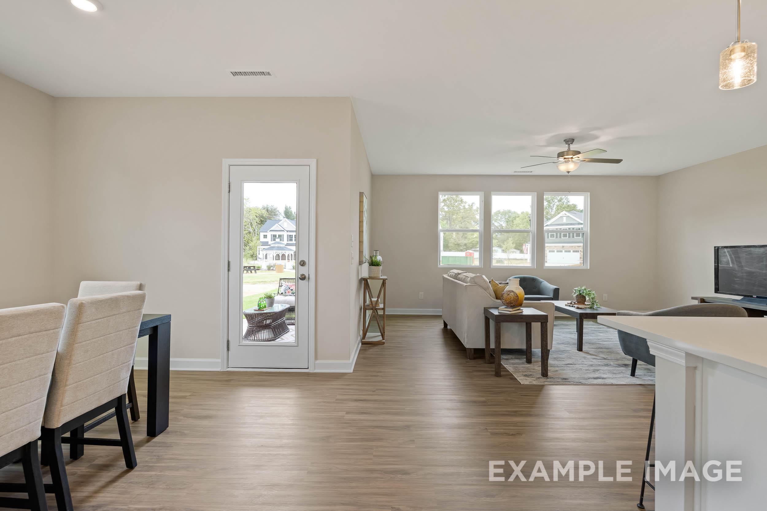 Open-concept living room and kitchen in The Preston B with neutral walls, wood floors, beige sofa, ceiling fan, and sliding door to backyard