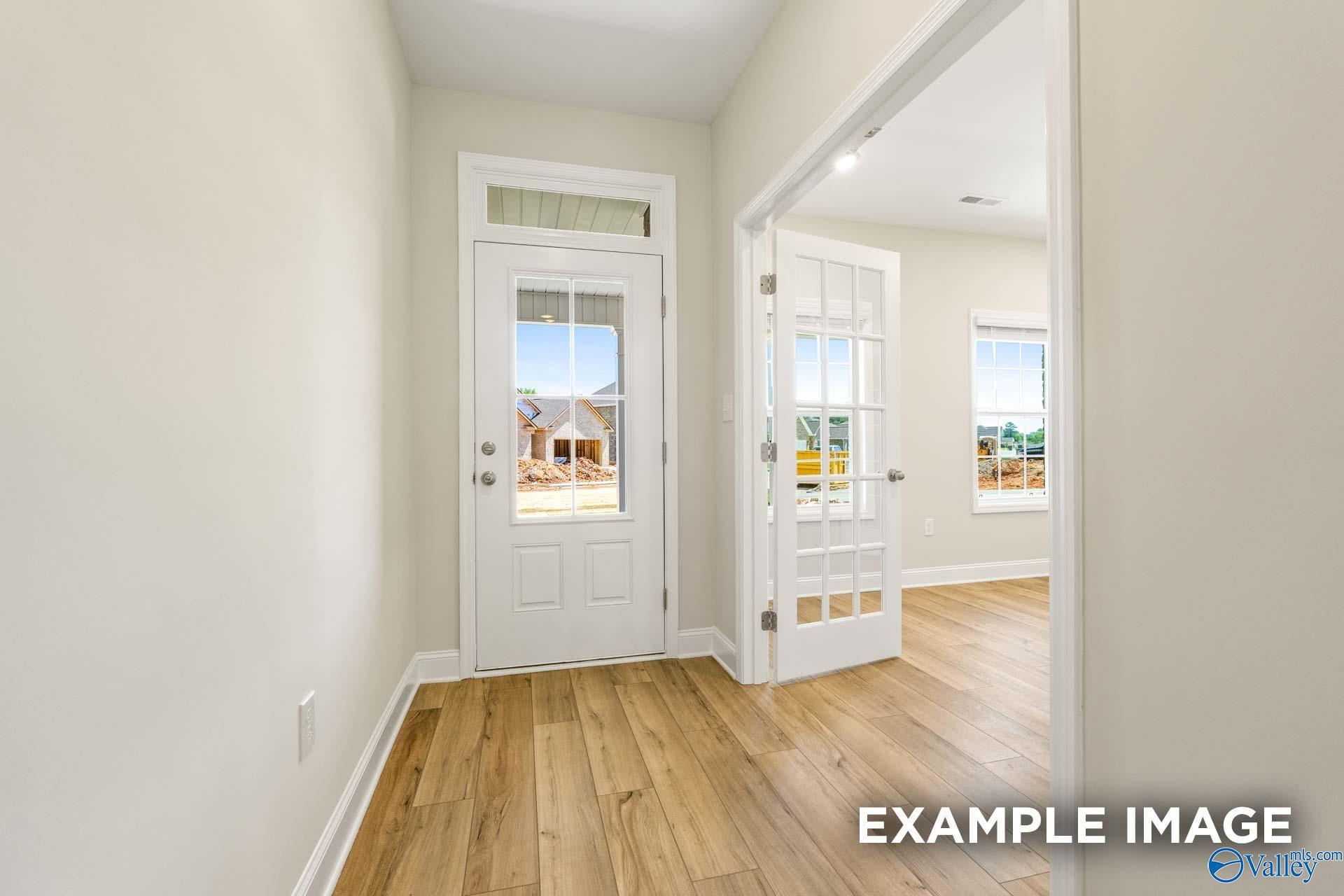 Bright foyer with white front door, glass French doors, and oak hardwood floors in Davidson Homes The Shelby B, Owens Cross Roads, Alabama