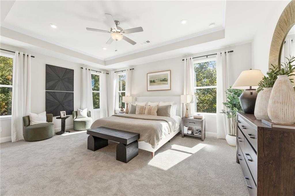 Elegant master bedroom with king bed, tray ceiling, large windows, and potted plants in Davidson Homes The Danbury C, Buford, GA