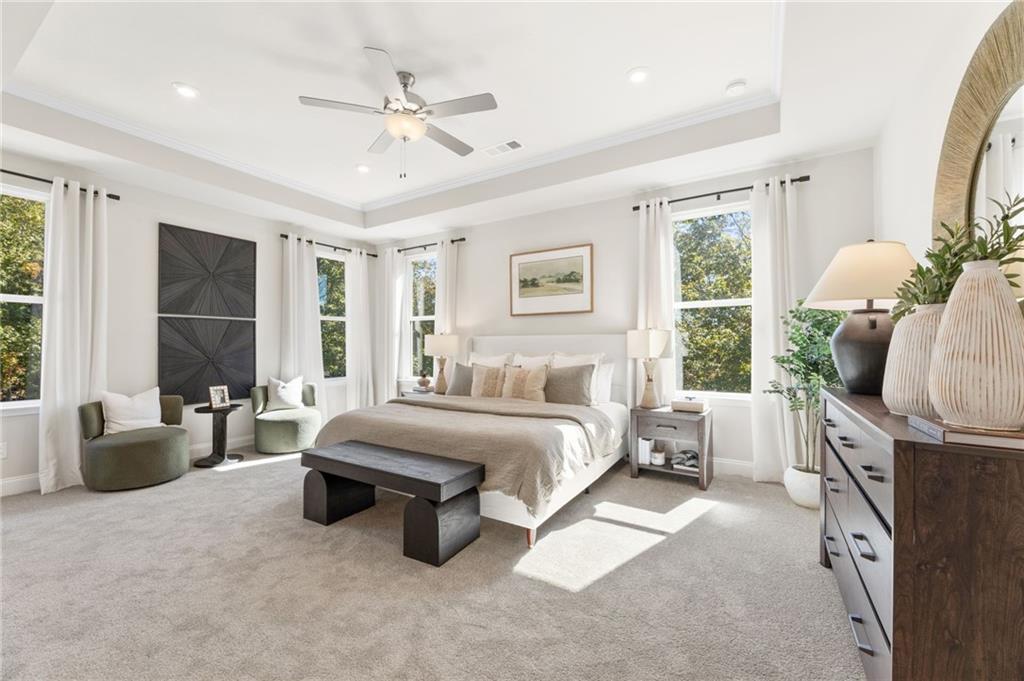 Elegant master bedroom with king bed, tray ceiling, large windows, and potted plants in Davidson Homes The Danbury C, Buford, GA