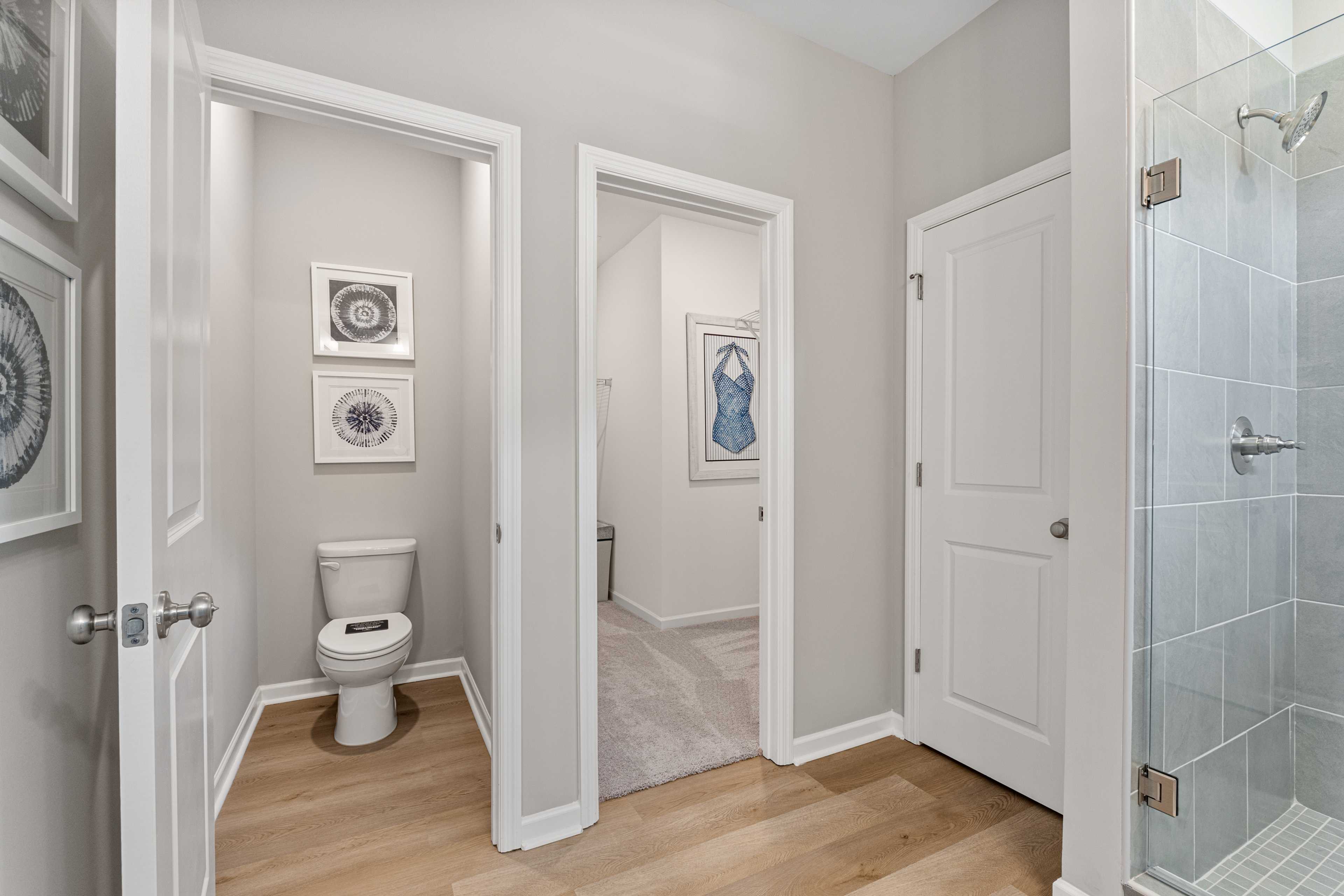 Modern primary bathroom in Forest Glen Hazel Green Alabama with glass walk-in shower, toilet, hardwood floors and framed art