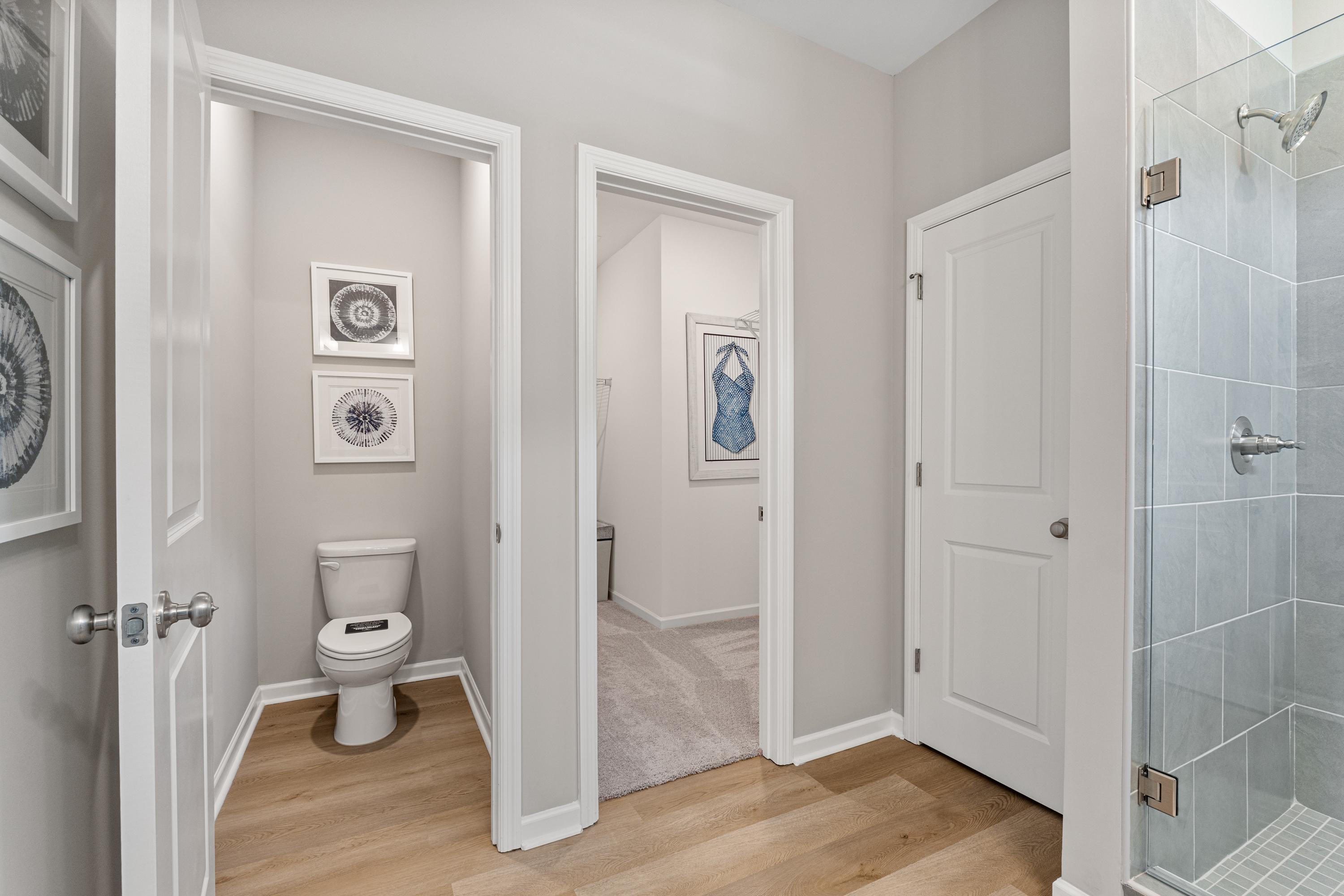 Modern primary bathroom in Forest Glen Hazel Green Alabama with glass walk-in shower, toilet, hardwood floors and framed art