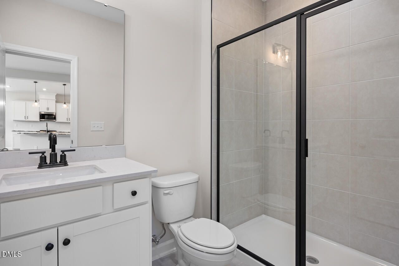 Modern bathroom with white vanity, glass-enclosed shower, and black fixtures in The Willow B home at Woodland Crossing.