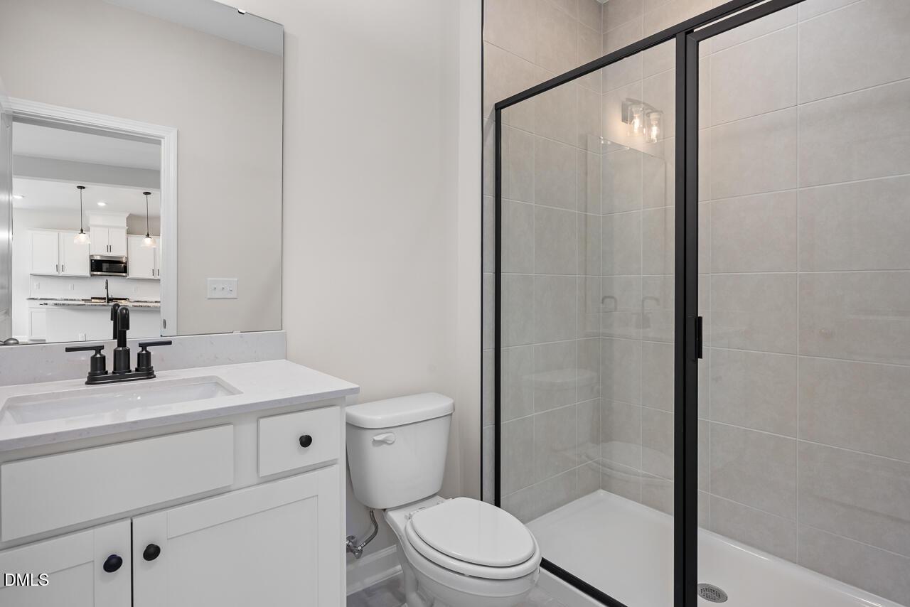 Modern bathroom with white vanity, glass-enclosed shower, and black fixtures in The Willow B home at Woodland Crossing.