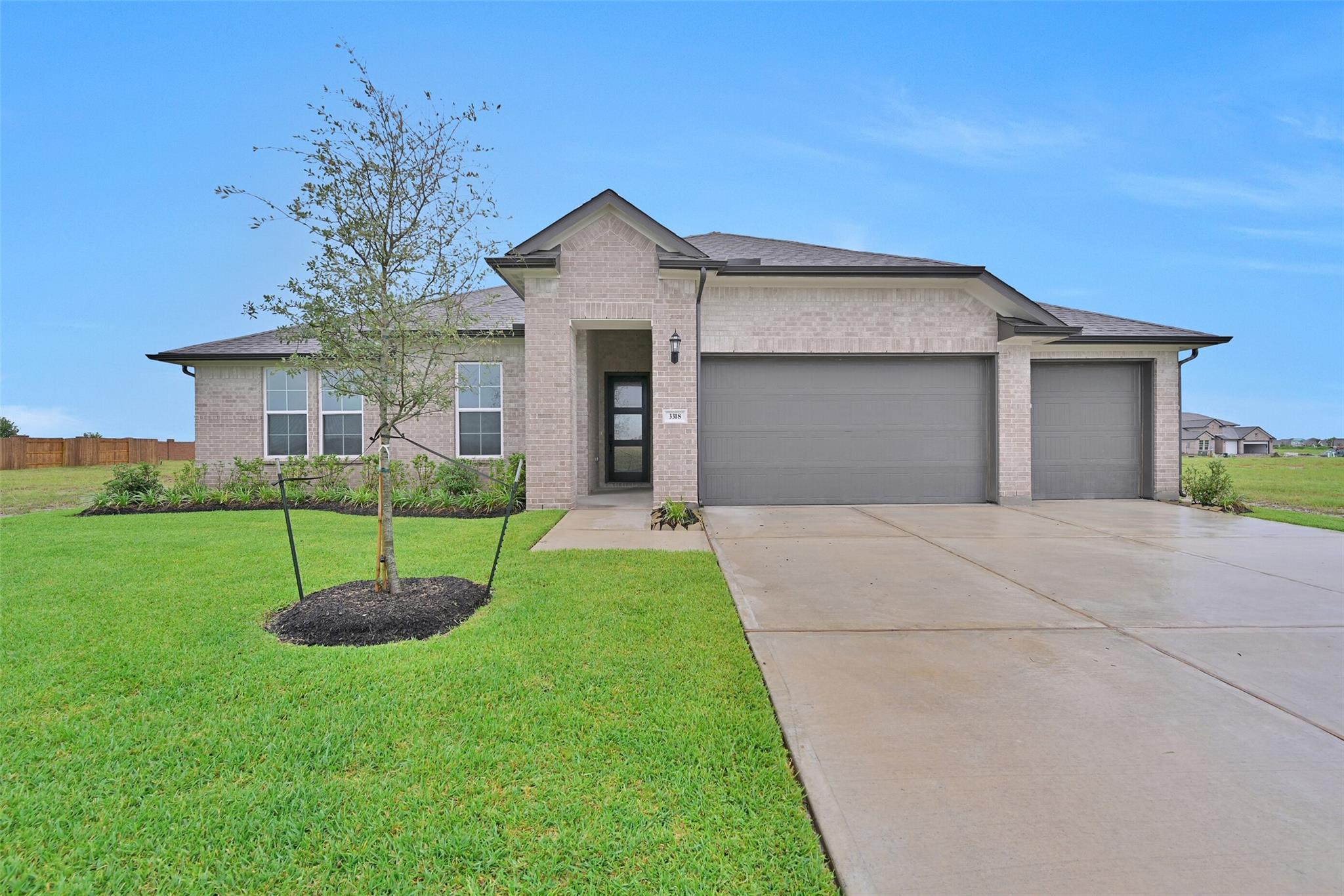 Modern brick single-story home with 3-car garage, front entry, young tree, and lush lawn in Lago Mar, Texas City