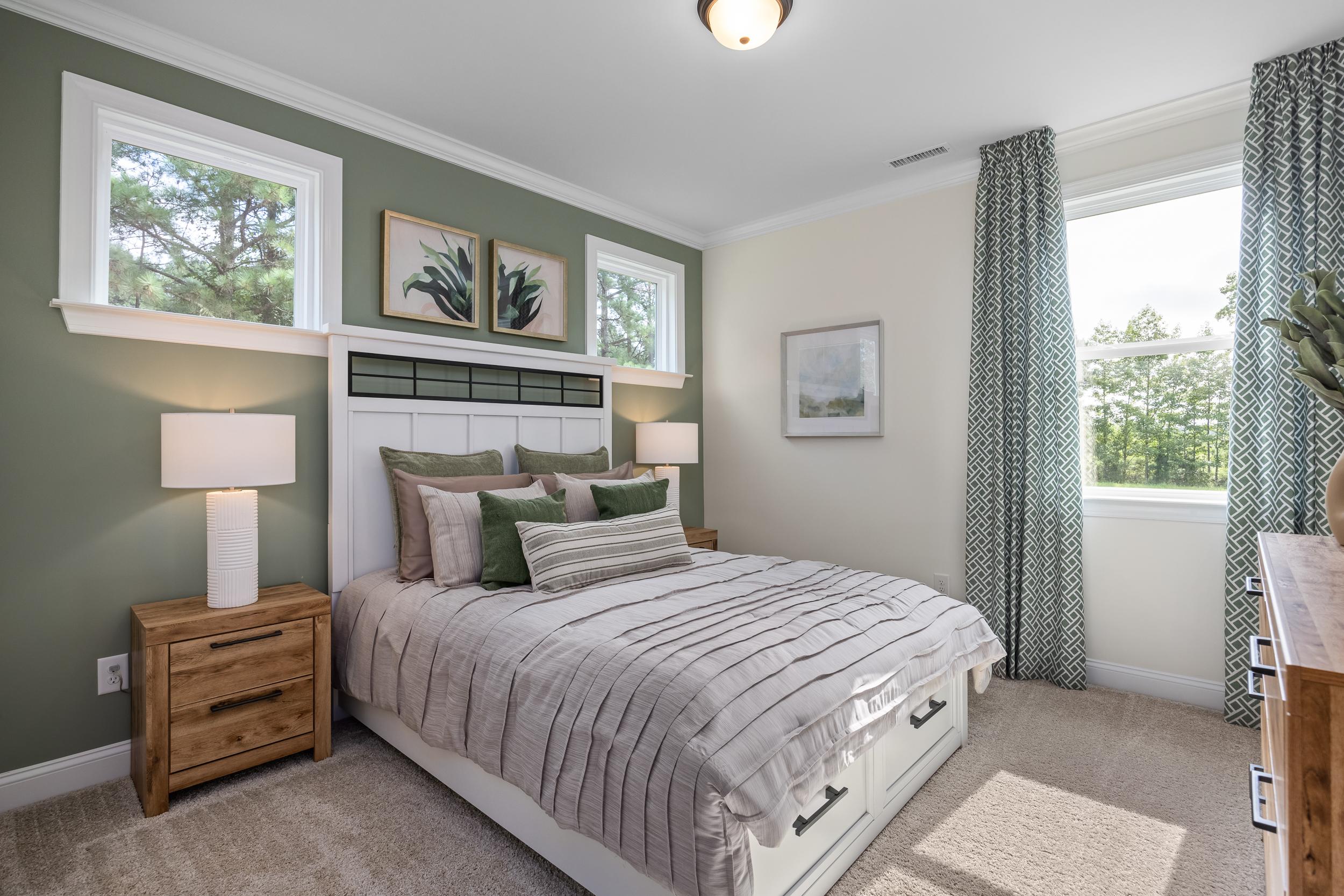 Spacious primary bedroom at Laneridge Estates in Raleigh NC with sage green accent wall, large tree-view windows, king bed, and modern wooden furniture