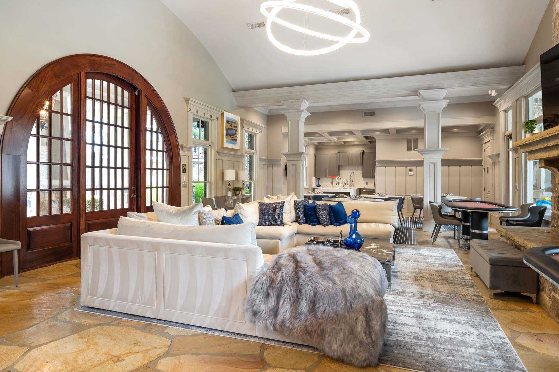 Spacious lounge in The Village at Towne Lake Woodstock GA featuring white sectional sofa, arched wooden doors, neon light fixture, and stone fireplace