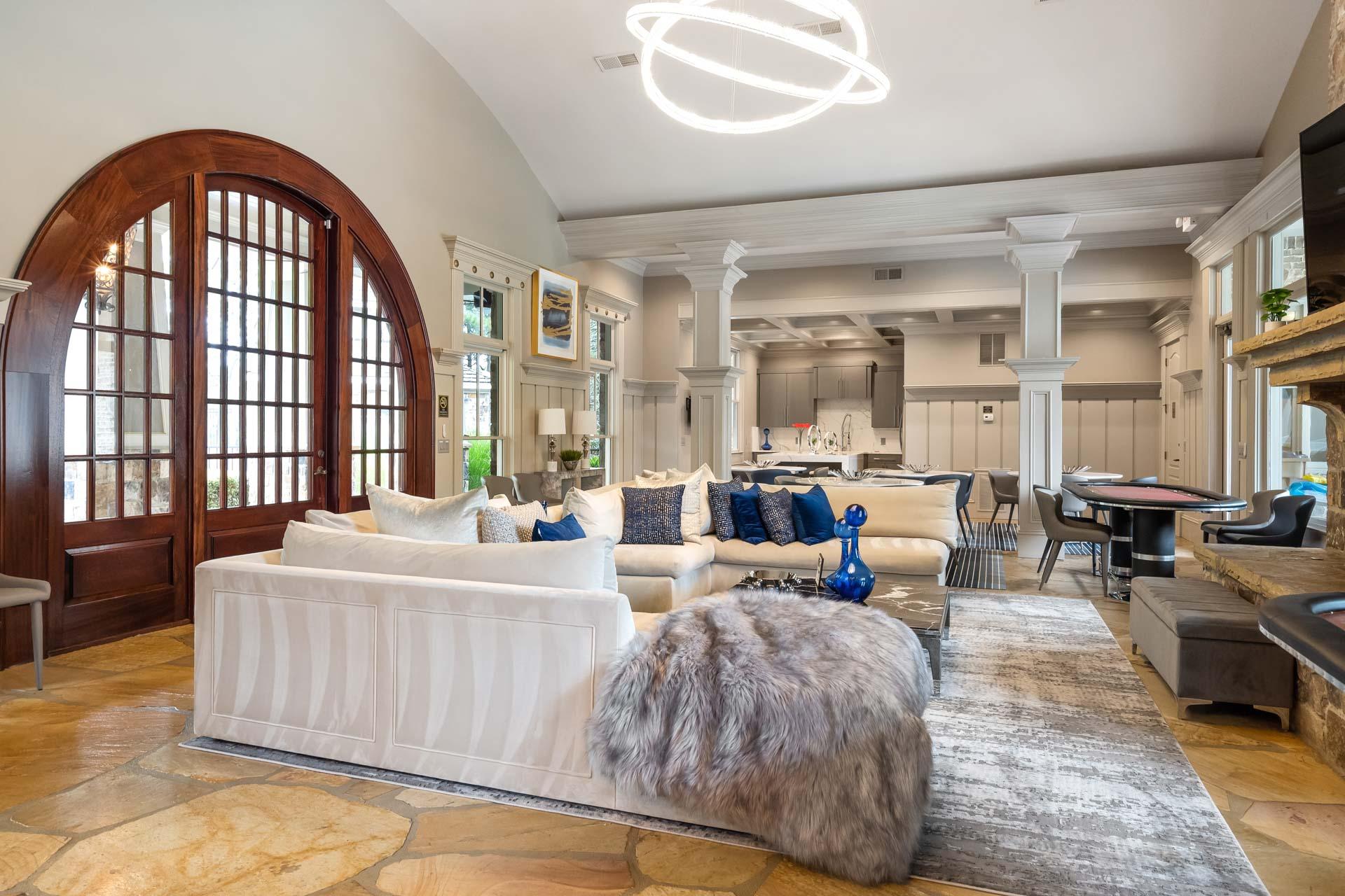 Spacious lounge in The Village at Towne Lake Woodstock GA featuring white sectional sofa, arched wooden doors, neon light fixture, and stone fireplace