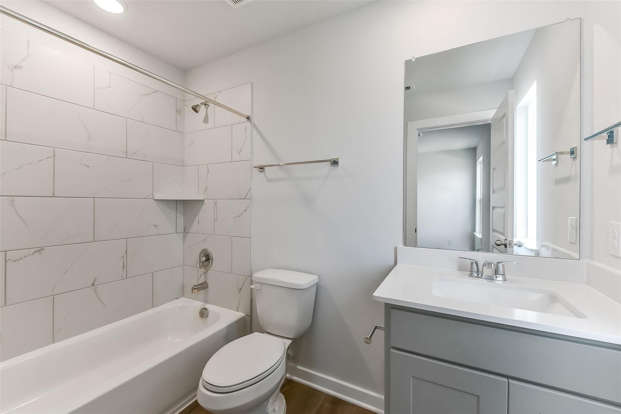 Elegant bathroom with marble-veined tile shower, deep soaking tub, white toilet, and gray vanity in Davidson Homes The Tierra C, Dayton Texas