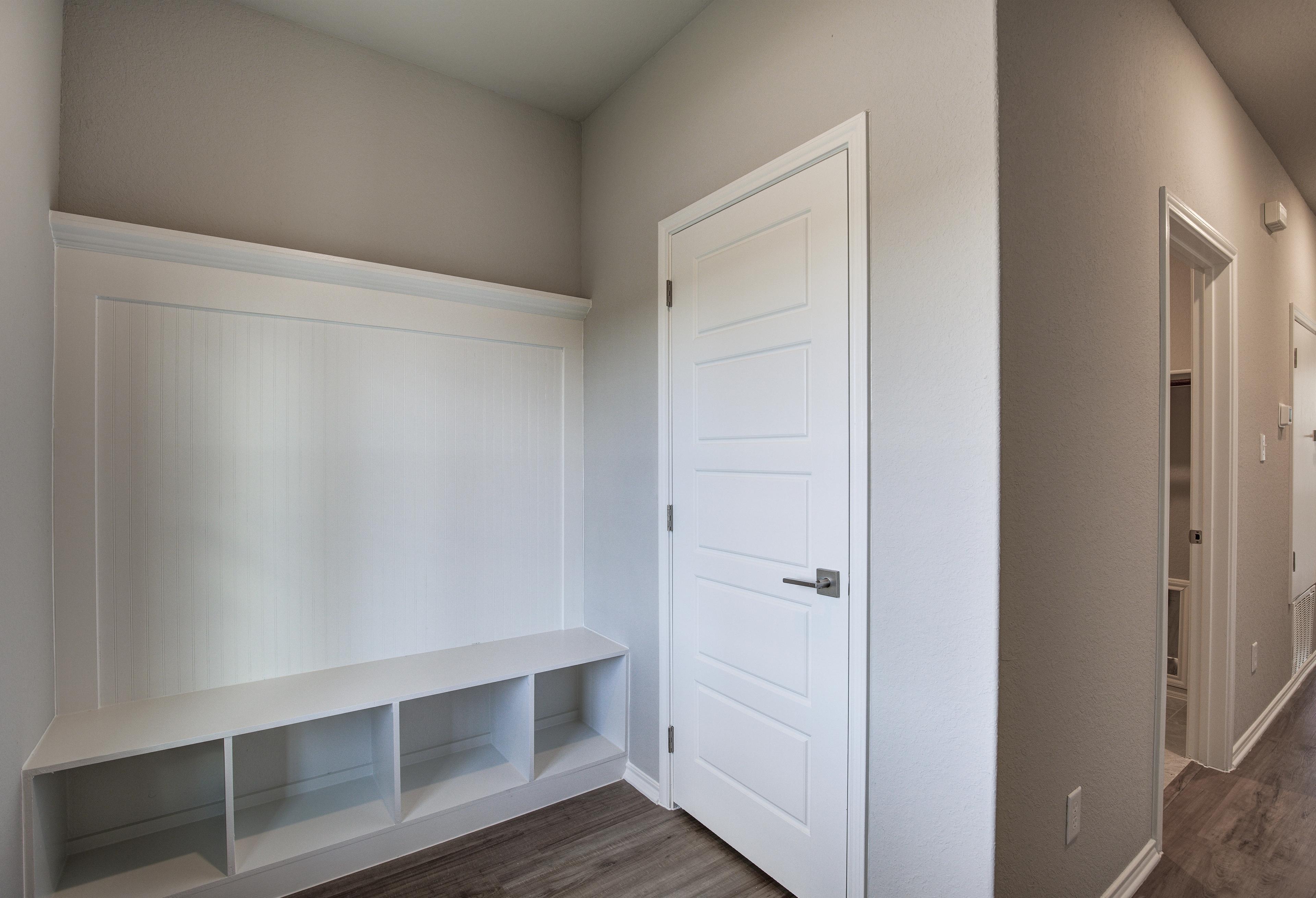Spacious mudroom in The Frio A with built-in white bench, cubby storage, paneled door, and hardwood hallway floors