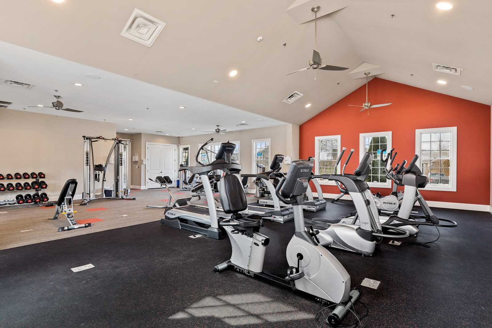 Spacious fitness center at Carellton in Gallatin, Tennessee featuring cardio machines, weight racks, red accent wall and rubber flooring