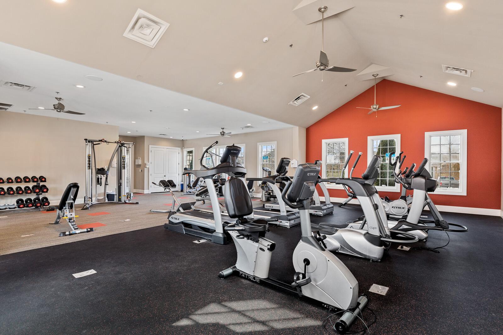 Spacious fitness center at Carellton in Gallatin, Tennessee featuring cardio machines, weight racks, red accent wall and rubber flooring