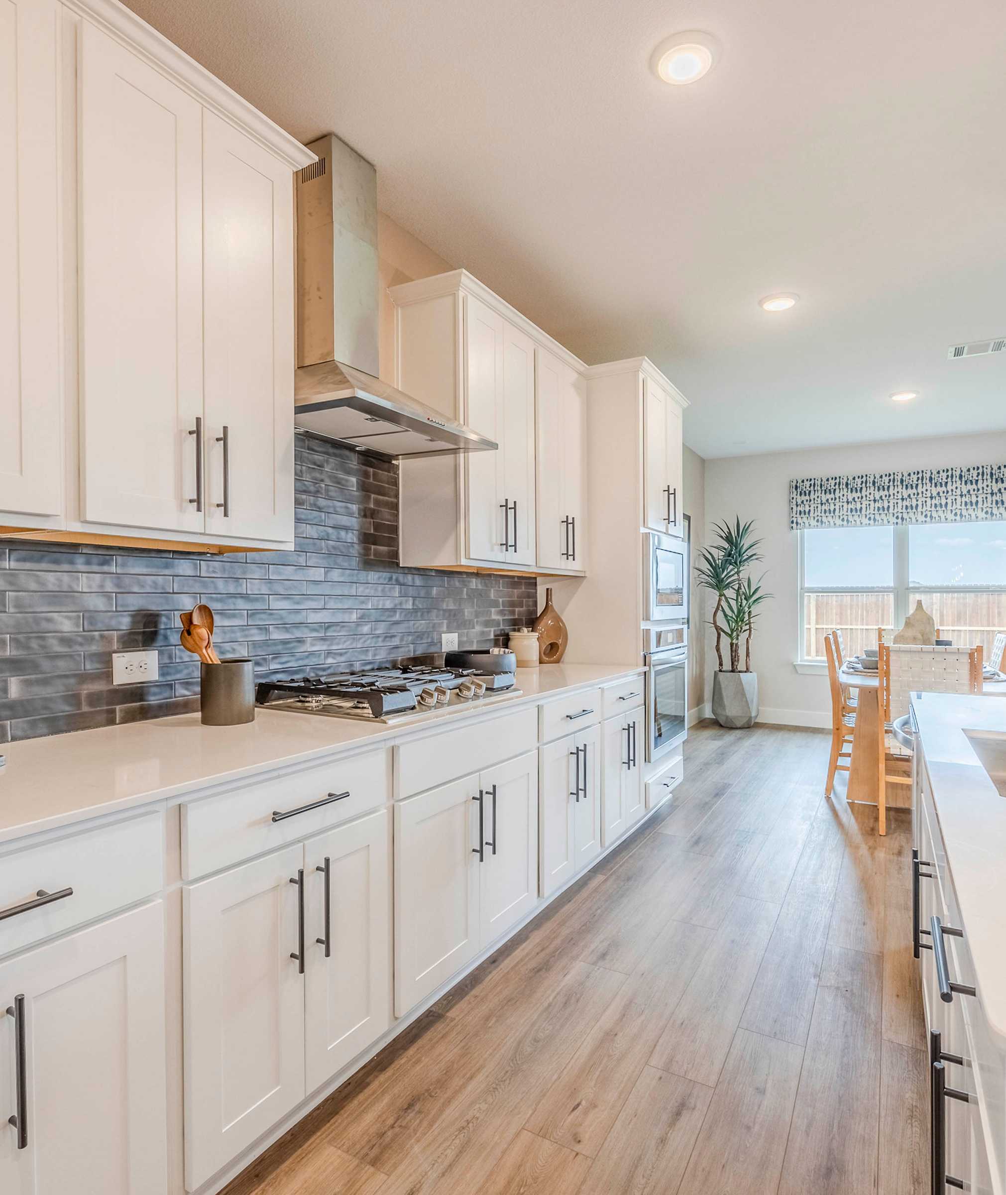 Open-concept kitchen at Waverly Estates in Josephine TX with white shaker cabinets, quartz counters, subway tile backsplash, hardwood floors, and dining area
