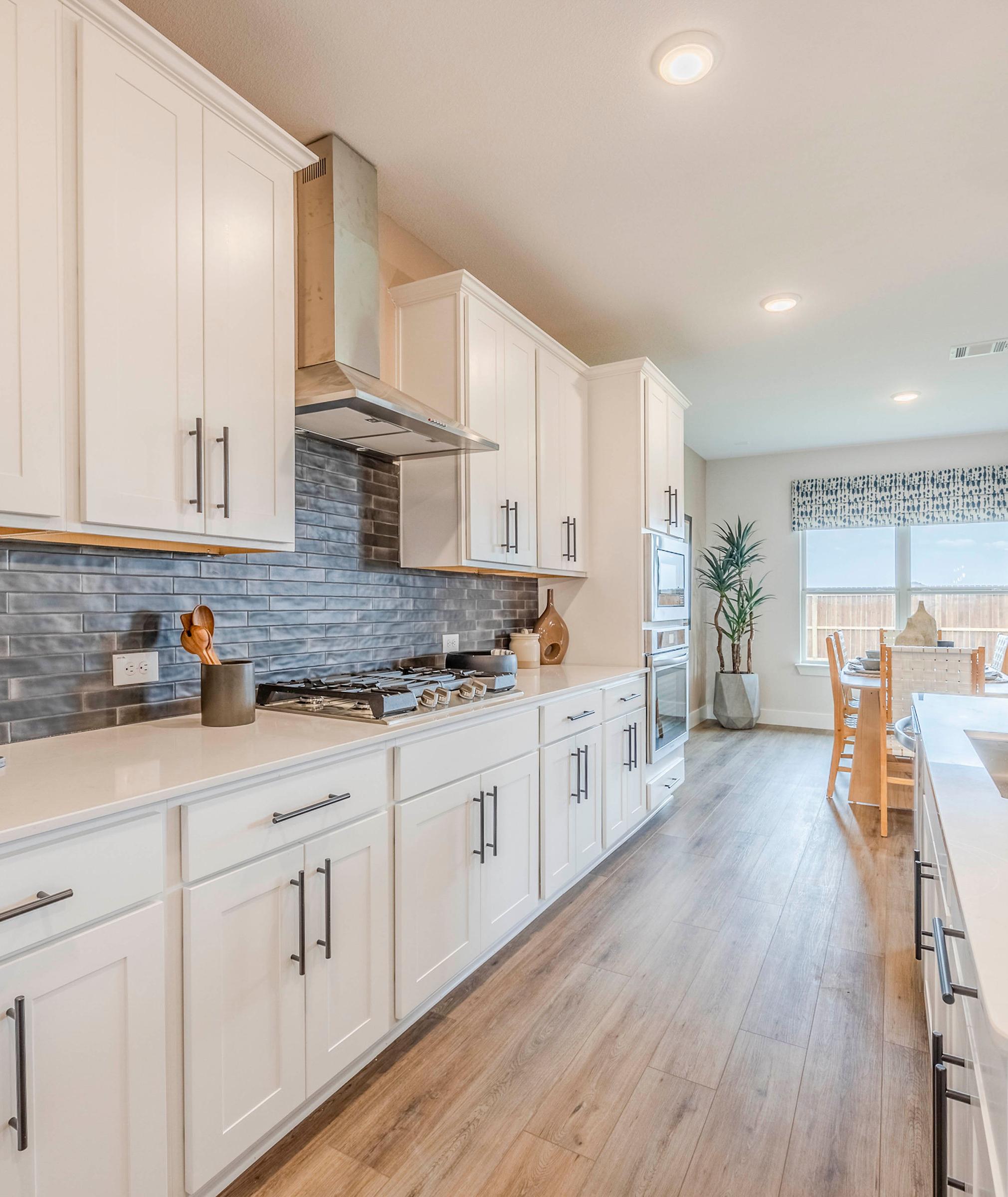 Open-concept kitchen at Waverly Estates in Josephine TX with white shaker cabinets, quartz counters, subway tile backsplash, hardwood floors, and dining area