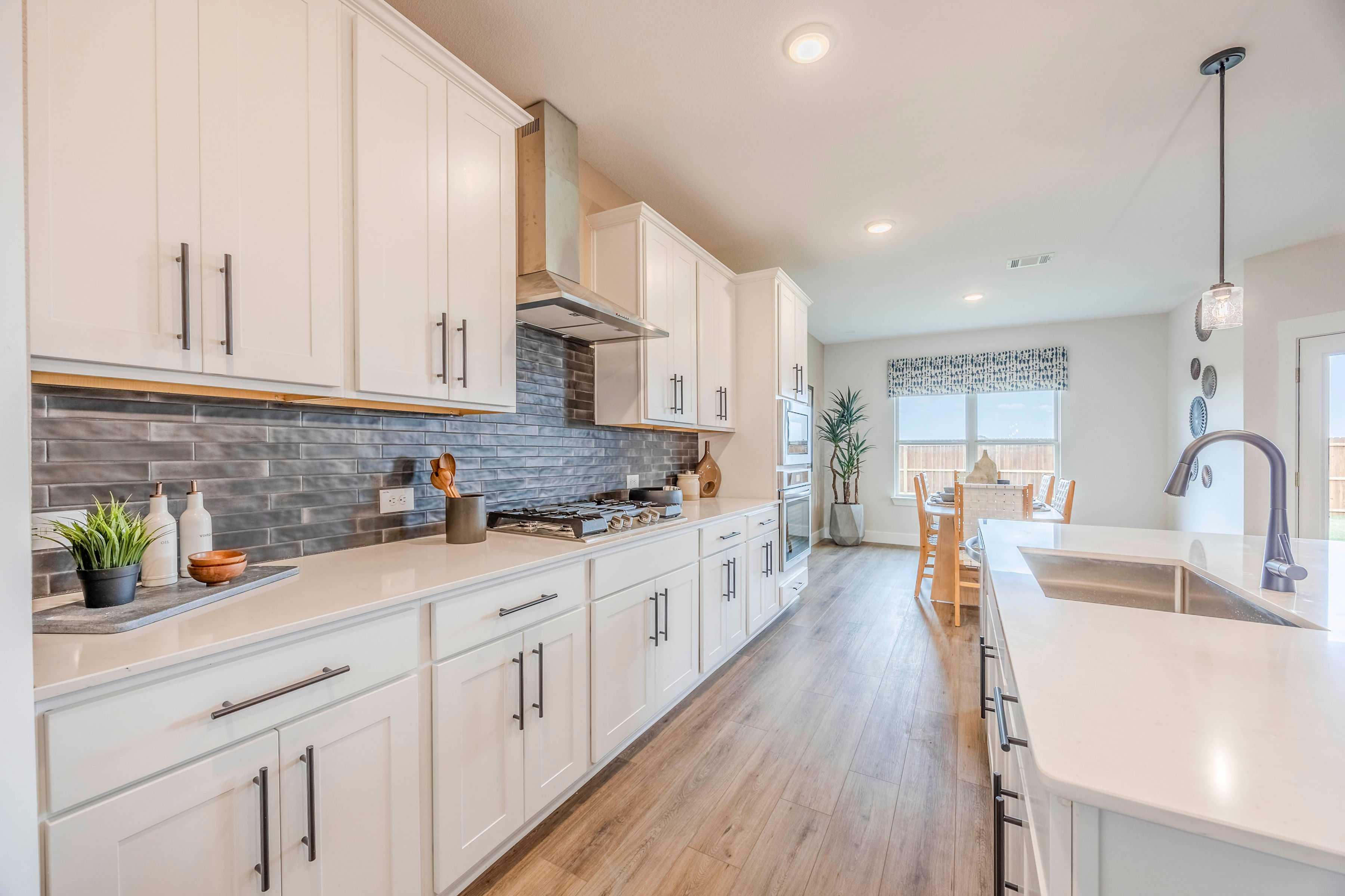Open-concept kitchen at Waverly Estates in Josephine TX with white shaker cabinets, quartz counters, subway tile backsplash, hardwood floors, and dining area