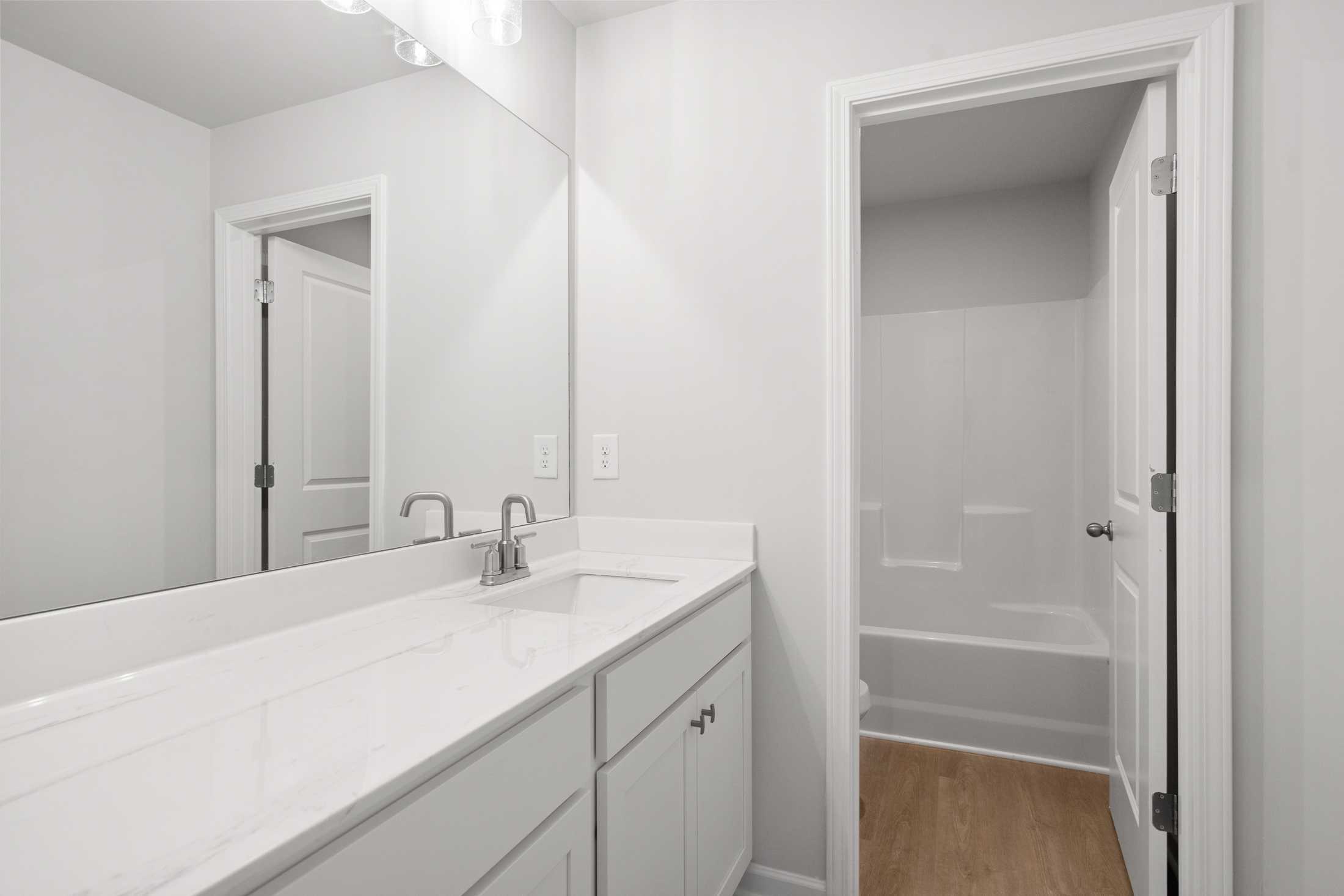 Spacious master bathroom in The Ash B at Wehunt Meadows featuring white vanity, double sink, large mirror, bathtub, and walk-in shower