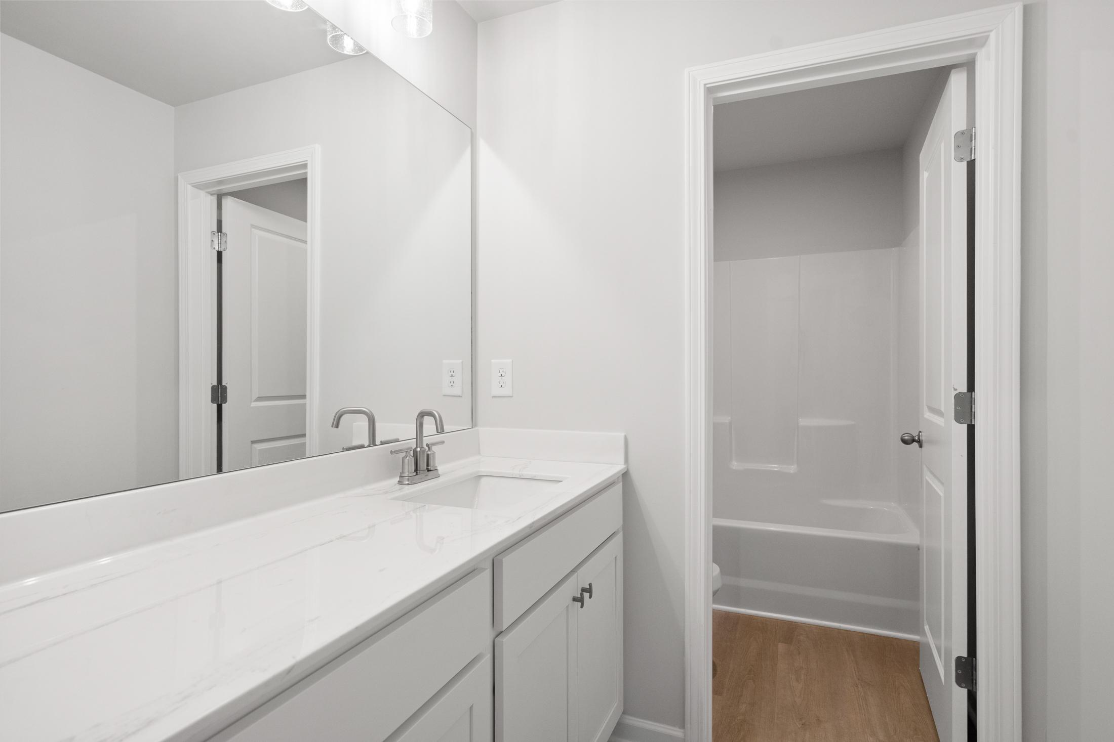 Spacious master bathroom in The Ash B at Wehunt Meadows featuring white vanity, double sink, large mirror, bathtub, and walk-in shower